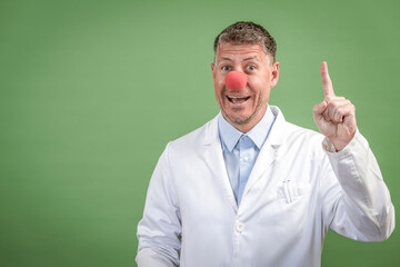 Scientist with white coat has red clown nose on and stands in front of green background