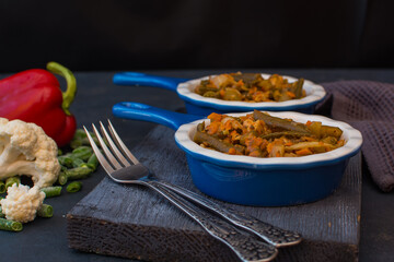 Vegetable stew with green beans and cauliflower and sweet peppers in a ceramic bowl on a wooden stand.
