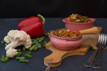 Vegetable stew with green beans and cauliflower and sweet peppers in a ceramic bowl on a wooden stand.
