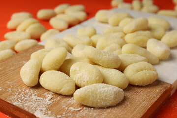 Cutting board with raw potato gnocchi on orange background