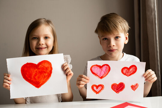 Kids painting red valetine heart card on table at home