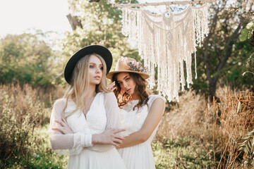 Fototapeta premium lesbian couple of beautiful young women in love in white wedding dresses posing on a meadow in the forest.