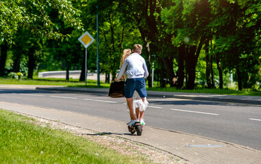 A guy and a girl rides an electric scooter in the summer Park
