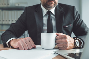 Businessman holding a white coffee cup at office desk. Coffee break for daily dose of caffeine