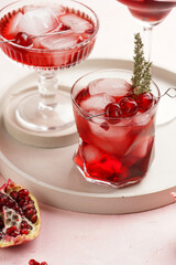 three glasses with fresh pomegranate juice with one real pomegranate on concrete tray on pink background