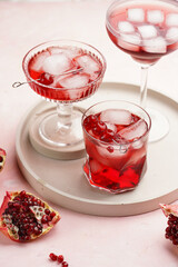 three glasses with fresh pomegranate juice with one real pomegranate on concrete tray on pink background