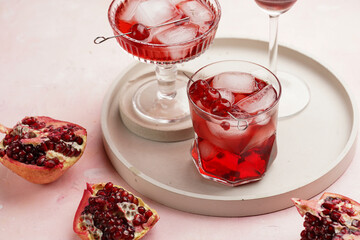 three glasses with fresh pomegranate juice with one real pomegranate on concrete tray on pink background