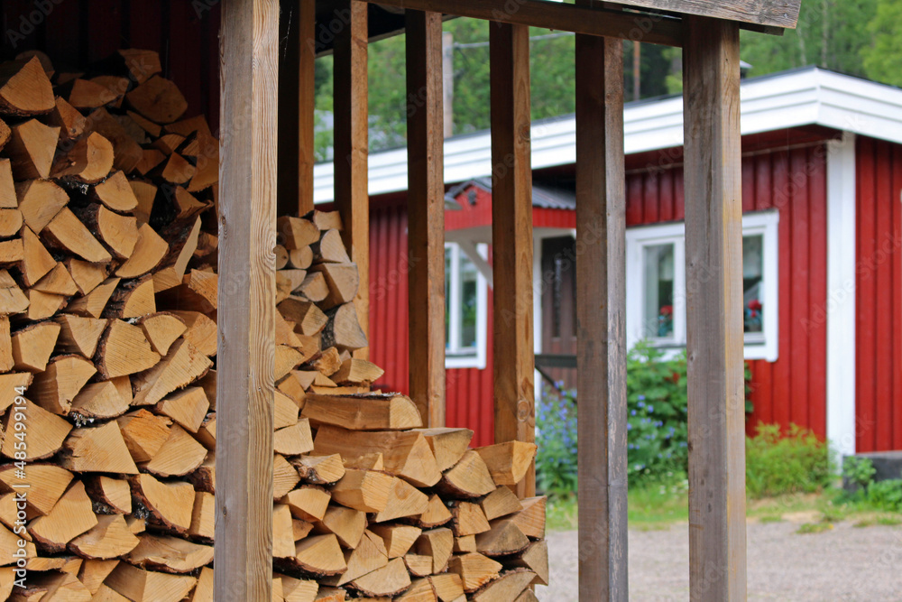 Sticker A closeup shot of firewood stock with a wooden red building on the background