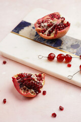 Fresh pomegranate cut in half and red seeds and cocktail cherries on marble board on pink background