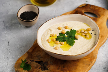 Hummus dip with chickpea and parsley in ceramic bowl on concrete surface with toasted baguette...