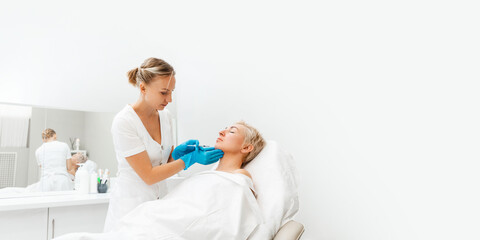 Cosmetologist in medical gloves with syringe injects filler in chin. Adult woman getting injection in the beauty salon. Web banner of cosmetology. Copy space