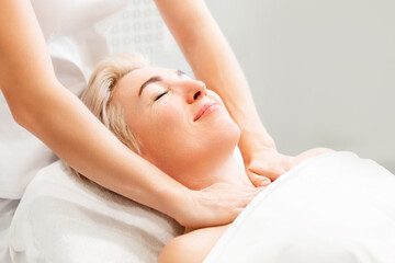 Portrait of an adult beautiful smiling woman at a massage session in a cosmetology clinic. The masseur performs the procedure on the neck and decollete area