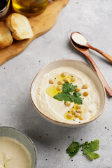 Hummus dip with chickpea and parsley in ceramic bowl on concrete surface with toasted baguette slices and olive oil on wooden board