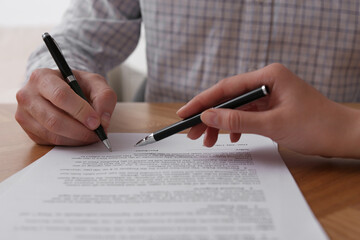 Fototapeta premium Businesspeople signing contract at wooden table, closeup of hands