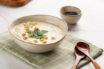 Hummus dip with chickpea and parsley in ceramic bowl on marble surface with toasted baguette slices and olive oil on wooden board