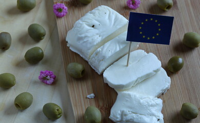 Traditional cheese called halloumi produces in Cyprus cut in slices, decorated with flag of European Union, green olives and pink small flowers, on cut board and wooden table