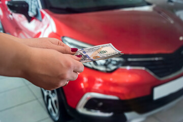 well-groomed female hands holding beautiful new dollar banknotes near cars