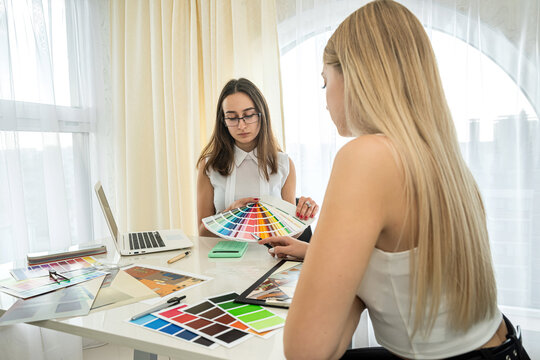 two beautiful girls designers sit at a table and choose colors for the design of rooms