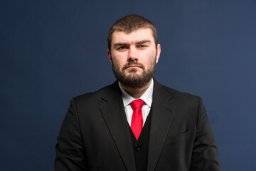 A businessman is preparing for a business meeting. A man in a business suit with a red tie on a blue background looks confidently at the camera