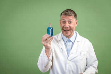 Scientist with white coat holding small flask with blue liquid and is standing in front of green background