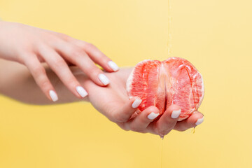Female elegant hands hold half a grapefruit. Oil is poured on top of the fruit. Copy space. The concept of sexuality - obrazy, fototapety, plakaty