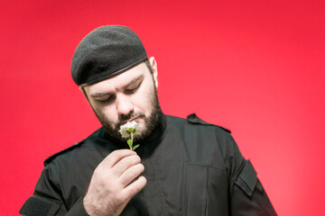 A male security guard in a black uniform and a cap holds a flower in his hand. Bodyguard. Defender of the law and order. Military. Mercenary. Handsome brutal man.