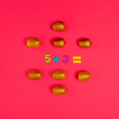 Mathematical task made of colorful numbers amd golden colored kiwis. Square flat lay composition on red background, minimal kids educational concept