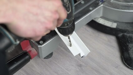 Close-up of male hands. A worker uses a cordless drill to drill a hole in a white plastic stick....