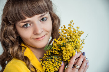 Naklejka premium close-up portrait of a young girl with very elegant makeup posing in the studio with a bouquet of cut flowers, mimosa.