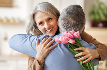 Happy senior woman receiving bouquet of spring flowers tulips from husband on Womens Day at home