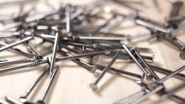 Metallic carpenter nails fall on a wooden furniture surface. Slow motion. Macro shot