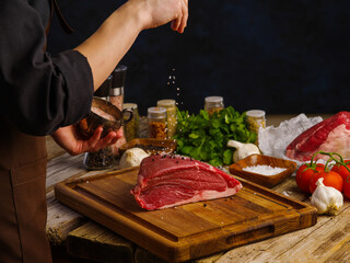 Cooking juicy steak from fresh organic meat from the farm by the chef's hands on a wooden cutting board. Dark background. Farming, restaurant, hotel, cafe, advertising.