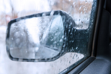 View of the rear view mirror on a rainy day from inside the car. Blurred view