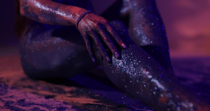 Woman with blue glitter on the body posing in a studio touching leg