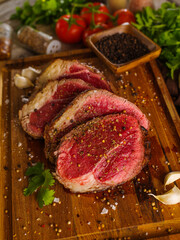 Raw steaks sprinkled with salt and spices on a wooden cutting board. Seasonings, herbs, garlic, pepper. Close-up. The concept is cooking meat steaks, restaurant, hotel, cafe, home cooking.