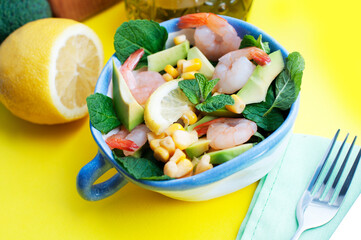 Salad with shrimps, avocado, corn and lemon with olive oil on a yellow background. Salad with shrimps and avocado on blue bowl on yellow background