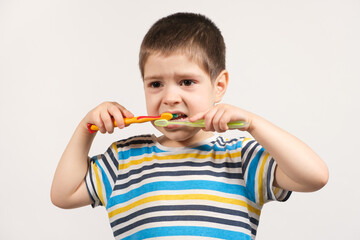 A preschooler boy brushes his teeth with two toothbrushes on a white background of isolate. Care for milk teeth in children