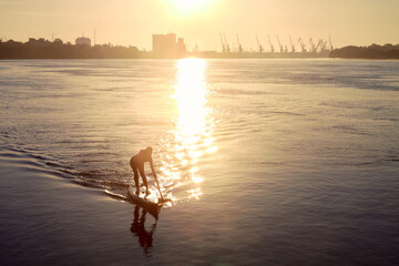 Silhouette of a young woman rowing on a SUP during a beautiful autumn sunrise on the river