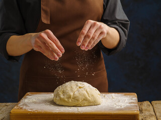 The chef sprinkles flour on the prepared dough on a wooden cutting board. Restaurant, hotel. cafe, bakery, confectionery, pizzeria, home cooking.