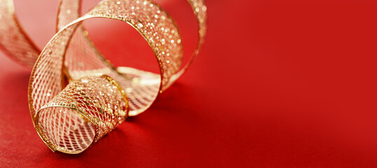 A swirl of golden gift ribbon on red for St Valentines day birthday gift or Christmas. Minimal with copy space. Mothers Day or wedding