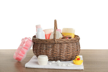 Wicker basket full of different baby cosmetic products, bathing accessories and toys on wooden table against white background