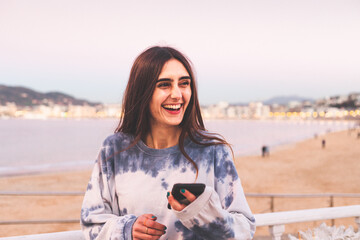 Fototapeta na wymiar Young caucasian woman using a smartphone at La Kontxa bay in Donostia-San Sebastian.