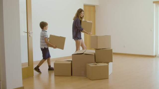 Excited family entering new house with cardboard boxes. Long shot of parents and kids putting carton boxes with stuff in pile in empty room, buying new apartment. Family moving, relocation concept