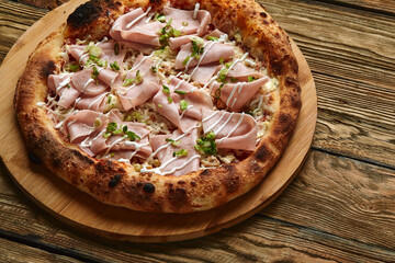 Fresh pizza with ham and pineapple on wooden table in restaurant.