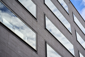 Modern building facade of residential and commercial premises. Rectangular large windows in gray house. Up view.