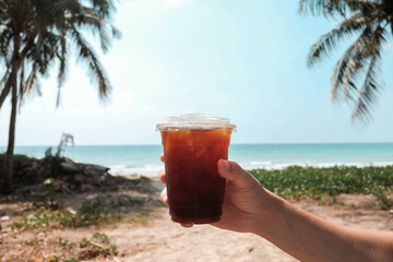 Hand holding iced coffee and sea, Iced black coffee americano in take away cup (plastic glass) on...