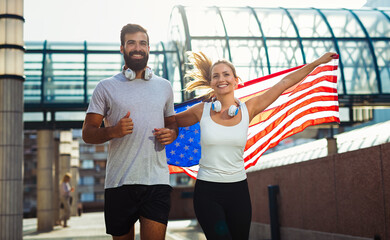Fototapeta na wymiar Portrait of young happy fitness couple exercising and having fun together outside with USA flag.