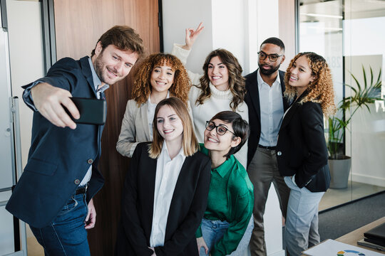 Smiling businessman taking selfie with colleagues through smart phone in office - Powered by Adobe