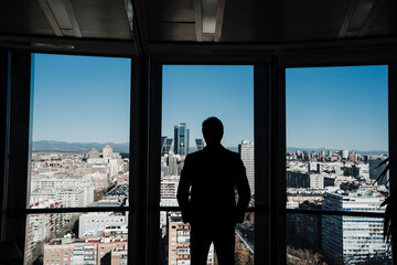 Silhouette of businessman standing with hands in pockets by glass wall