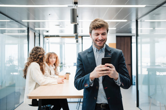 Smiling businessman text messaging through smart phone in office